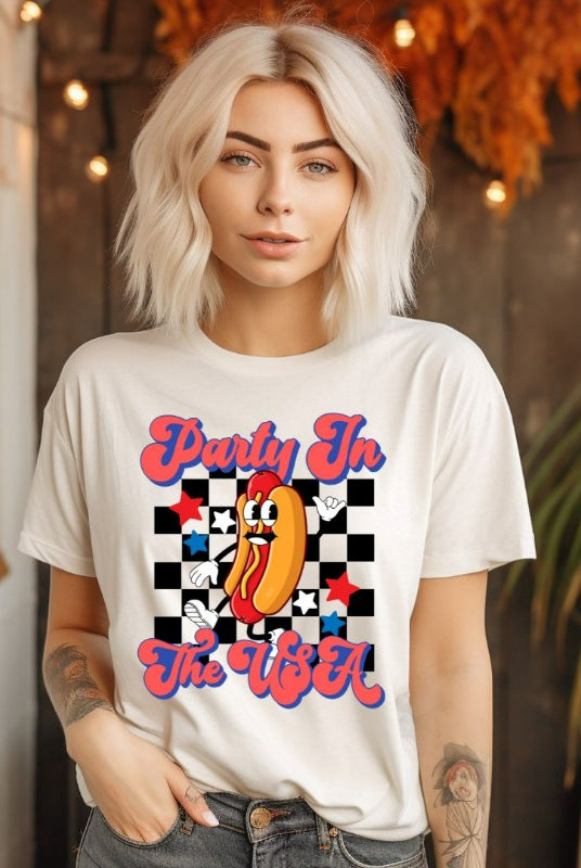 Graphic of a retro-style hotdog with a checkered background, with the text 'Party in the USA' on the front of a white graphic tee.