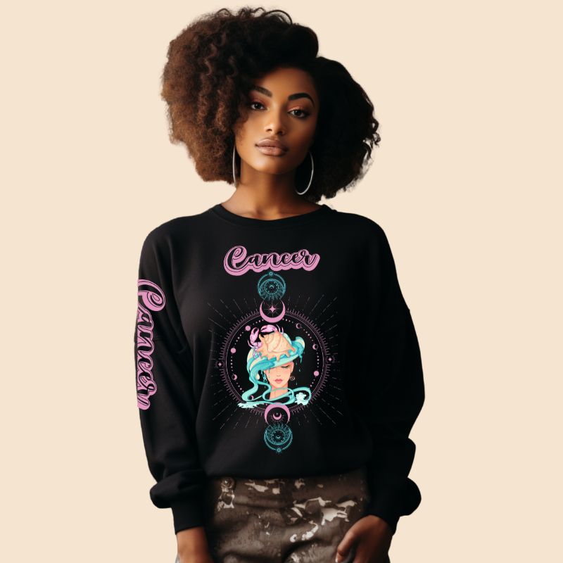 Black Gildan sweatshirt featuring a vibrant Cancer zodiac design. The front showcases an artistic representation of a woman with flowing hair adorned with a crab, surrounded by celestial elements like moons and stars, in pastel colors. The word "Cancer" is written in a stylish pink script above the design. The sleeve also has "Cancer" written vertically in matching pink script.