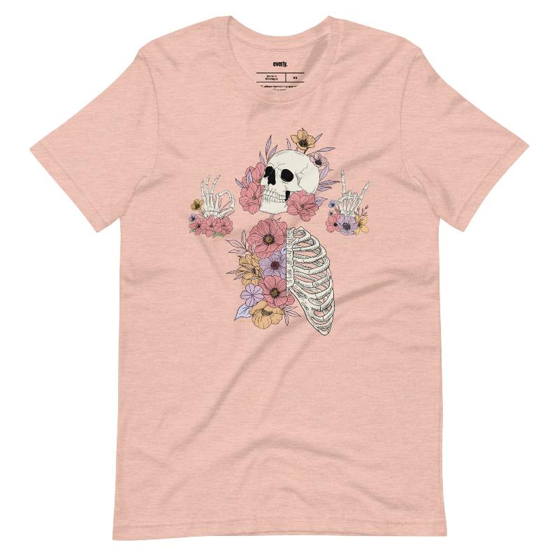 Peach t-shirt featuring a detailed skeleton design with ribcage and hands intertwined with soft, colorful flowers, blending gothic and floral aesthetics.