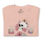 Peach t-shirt featuring a detailed skeleton design with ribcage and hands intertwined with soft, colorful flowers, blending gothic and floral aesthetics.