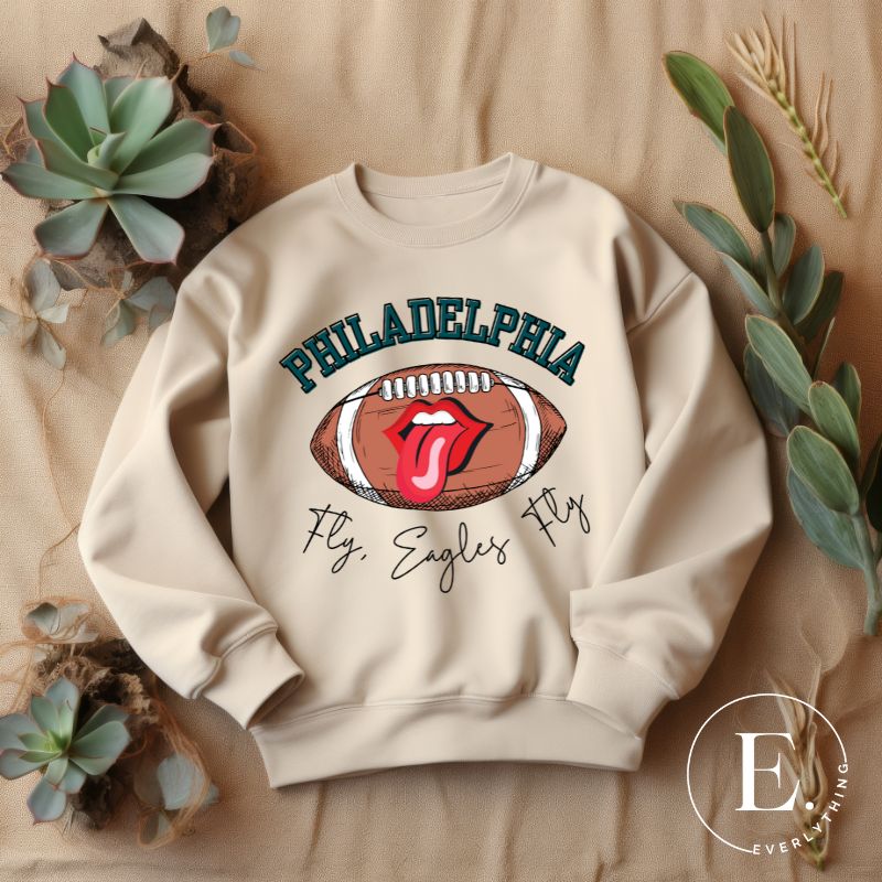 Show your support for the Philadelphia Eagles with this stylish sweatshirt, featuring a football and fun lips and tongue design. Complete with the team's iconic slogan "Fly Eagles Fly" and the distinctive Philadelphia wordmark, on a sand colored sweatshirt. 