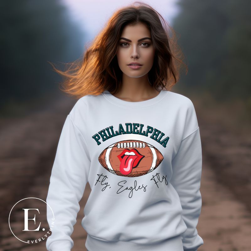 Show your support for the Philadelphia Eagles with this stylish sweatshirt, featuring a football and fun lips and tongue design. Complete with the team's iconic slogan "Fly Eagles Fly" and the distinctive Philadelphia wordmark, on a white sweatshirt. 