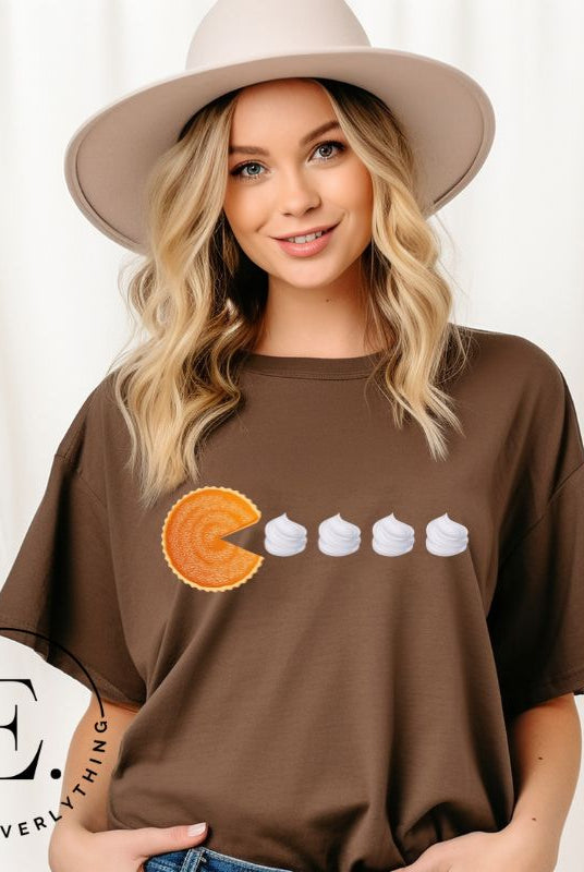 Level up your style with our playful t-shirt featuring a pumpkin pie shaped like Pac-Man devouring whipped cream swirls on a brown shirt. 