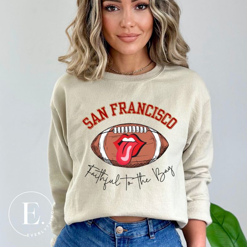 Show you allegiance to the San Francisco 49ers with this trendy sweatshirt, featuring a football and playful lips and tongue design. Emblazoned with the team's slogan "Faithful to the Bay" and the iconic San Francisco wordmark, on a sand colored sweatshirt. 