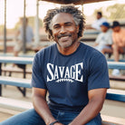 "Savage" in large, bold white letters with a football graphic underneath. The shirt is from Bella + Canvas and is made of 100% combed and ring-spun cotton on a navy shirt