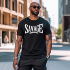 "Savage" in large, bold white letters with a football graphic underneath. The shirt is from Bella + Canvas and is made of 100% combed and ring-spun cotton on a black shirt