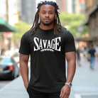 "Savage" in large, bold white letters with a football graphic underneath. The shirt is from Bella + Canvas and is made of 100% combed and ring-spun cotton on a black shirt