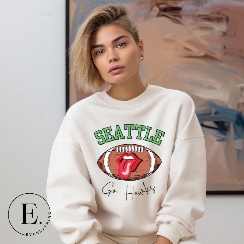Support the Seattle Seahawks in style with this unique sweatshirt featuring a football and playful lips and tongue design. Featuring the team's slogan "Go Hawks" and the iconic Seattle wordmark, on a white sweatshirt. 