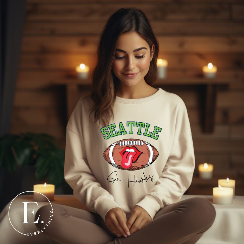 Support the Seattle Seahawks in style with this unique sweatshirt featuring a football and playful lips and tongue design. Featuring the team's slogan "Go Hawks" and the iconic Seattle wordmark, on a sand colored sweatshirt. 
