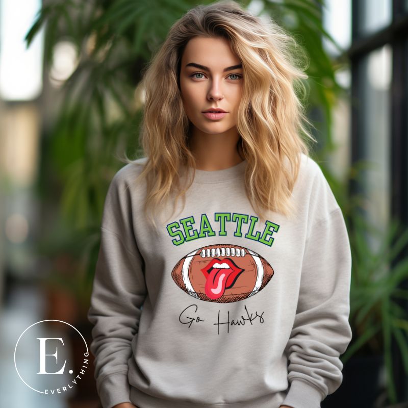 Support the Seattle Seahawks in style with this unique sweatshirt featuring a football and playful lips and tongue design. Featuring the team's slogan "Go Hawks" and the iconic Seattle wordmark, on a grey sweatshirt. 