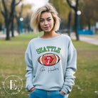 Support the Seattle Seahawks in style with this unique sweatshirt featuring a football and playful lips and tongue design. Featuring the team's slogan "Go Hawks" and the iconic Seattle wordmark, on a light blue sweatshirt. 