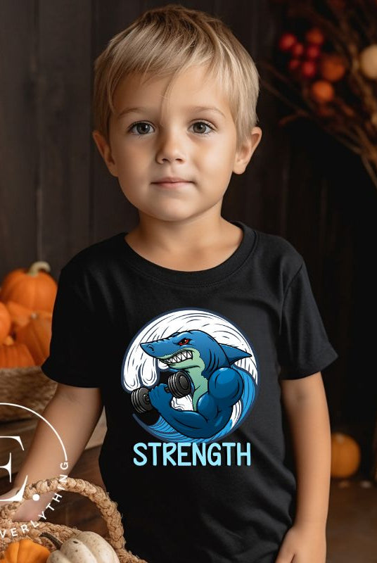 Dive into strength and style with our kids' shirt. Featuring a shark lifting weights with the empowering word 'strength' underneath on a black shirt. 