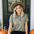 Embrace the enchanting night sky with our captivating t-shirt. Featuring a crescent moon, stars, and a spiderweb with three adorable spiders hanging down on the front pocket on a green shrit. 