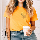 Embrace the enchanting night sky with our captivating t-shirt. Featuring a crescent moon, stars, and a spiderweb with three adorable spiders hanging down on the front pocket on an orange shirt. 