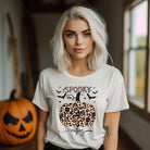 White t-shirt featuring a leopard-print pumpkin and "Spooky Vibes" text surrounded by bats, perfect for Halloween and fall season style.