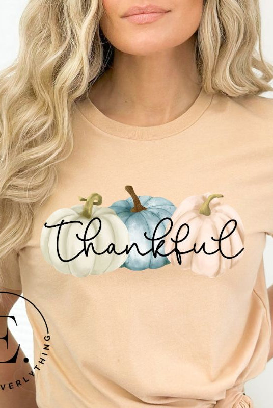 Express gratitude in style with our charming t-shirt. This design radiates autumn appreciation, featuring three pastel pumpkins and the word 'thankful' gracefully woven through the middle on a peach shirt. 