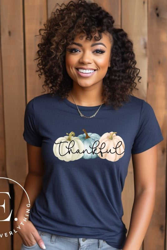 Express gratitude in style with our charming t-shirt. This design radiates autumn appreciation, featuring three pastel pumpkins and the word 'thankful' gracefully woven through the middle on a navy shirt. 