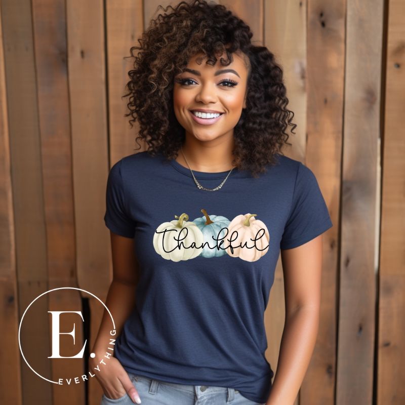 Express gratitude in style with our charming t-shirt. This design radiates autumn appreciation, featuring three pastel pumpkins and the word 'thankful' gracefully woven through the middle on a navy shirt. 