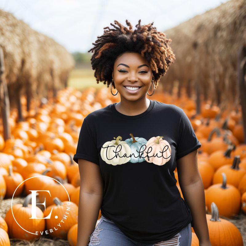 Express gratitude in style with our charming t-shirt. This design radiates autumn appreciation, featuring three pastel pumpkins and the word 'thankful' gracefully woven through the middle on a black shirt. 