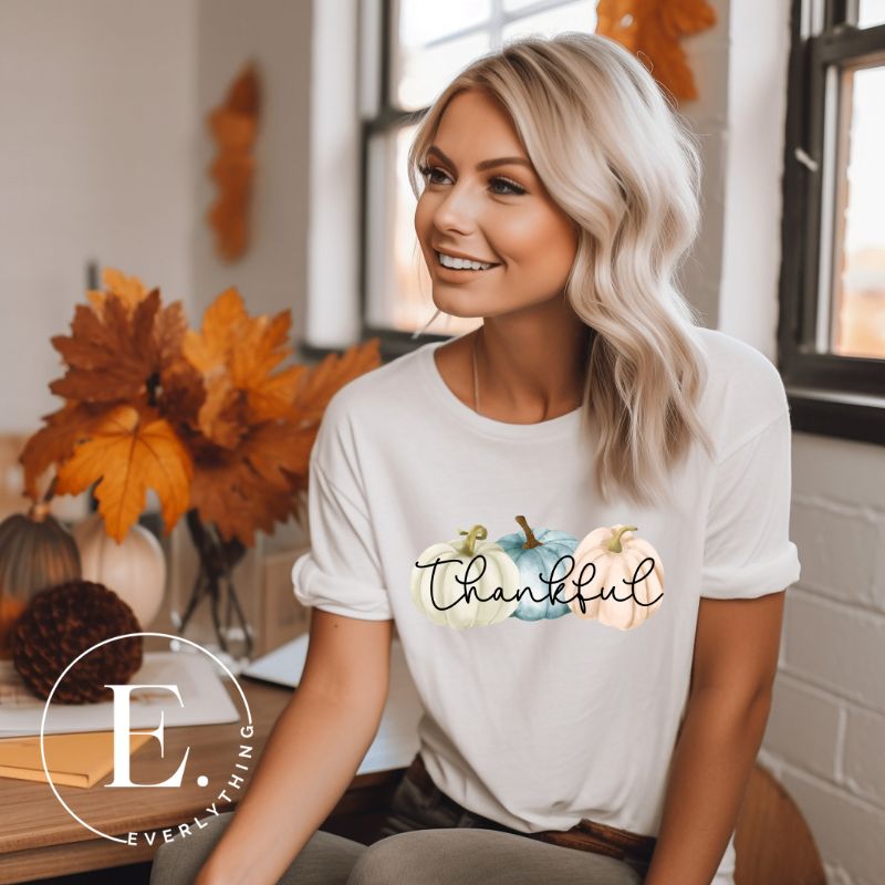 Express gratitude in style with our charming t-shirt. This design radiates autumn appreciation, featuring three pastel pumpkins and the word 'thankful' gracefully woven through the middle on a white shirt. 
