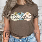 Express gratitude in style with our charming t-shirt. This design radiates autumn appreciation, featuring three pastel pumpkins and the word 'thankful' gracefully woven through the middle on a brown shirt. 