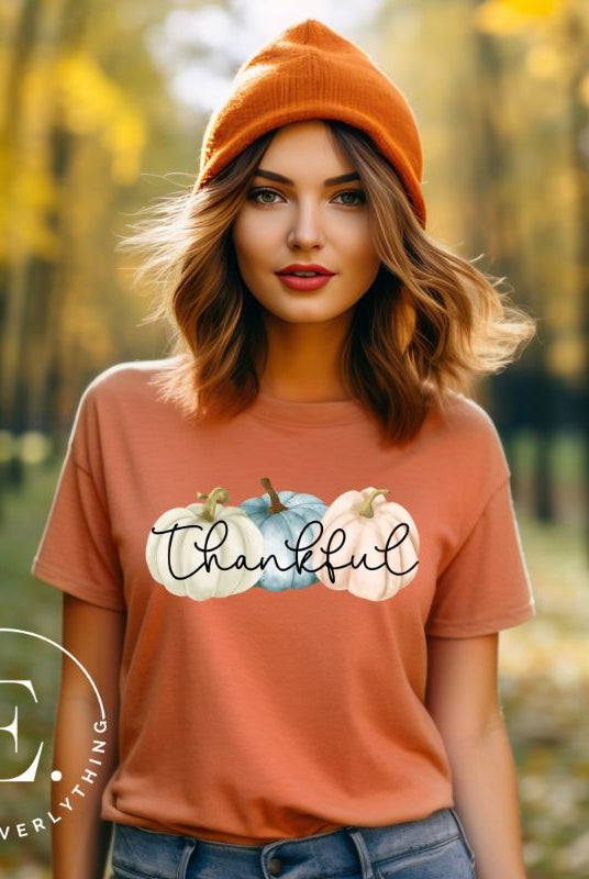 Express gratitude in style with our charming t-shirt. This design radiates autumn appreciation, featuring three pastel pumpkins and the word 'thankful' gracefully woven through the middle on an orange shirt. 