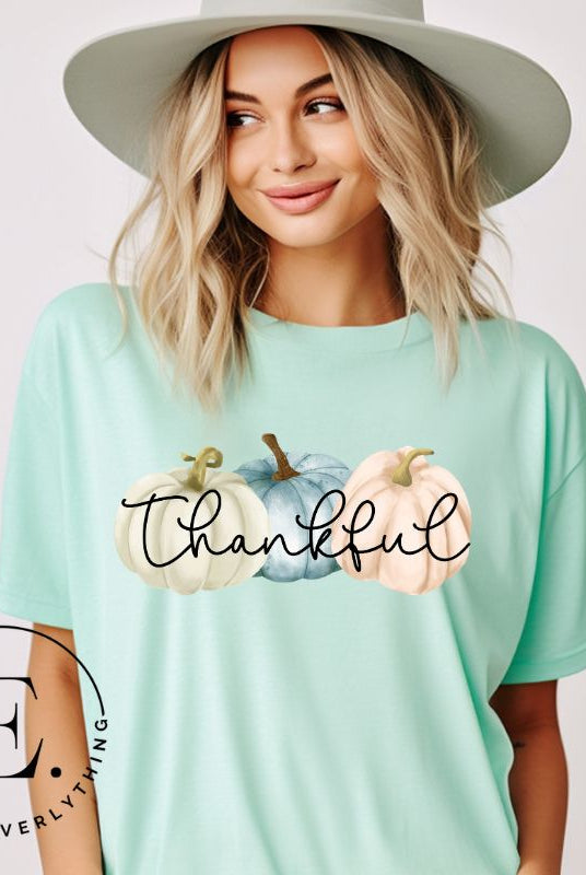 Express gratitude in style with our charming t-shirt. This design radiates autumn appreciation, featuring three pastel pumpkins and the word 'thankful' gracefully woven through the middle on a mint shirt. 