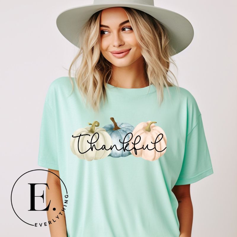 Express gratitude in style with our charming t-shirt. This design radiates autumn appreciation, featuring three pastel pumpkins and the word 'thankful' gracefully woven through the middle on a mint shirt. 