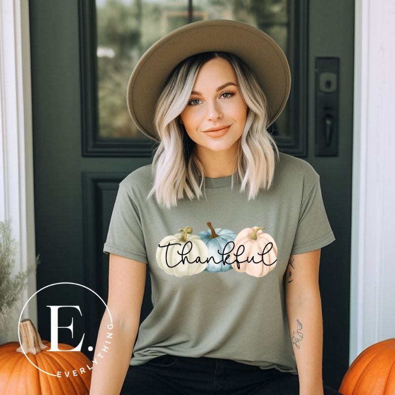 Express gratitude in style with our charming t-shirt. This design radiates autumn appreciation, featuring three pastel pumpkins and the word 'thankful' gracefully woven through the middle on a green shirt. 