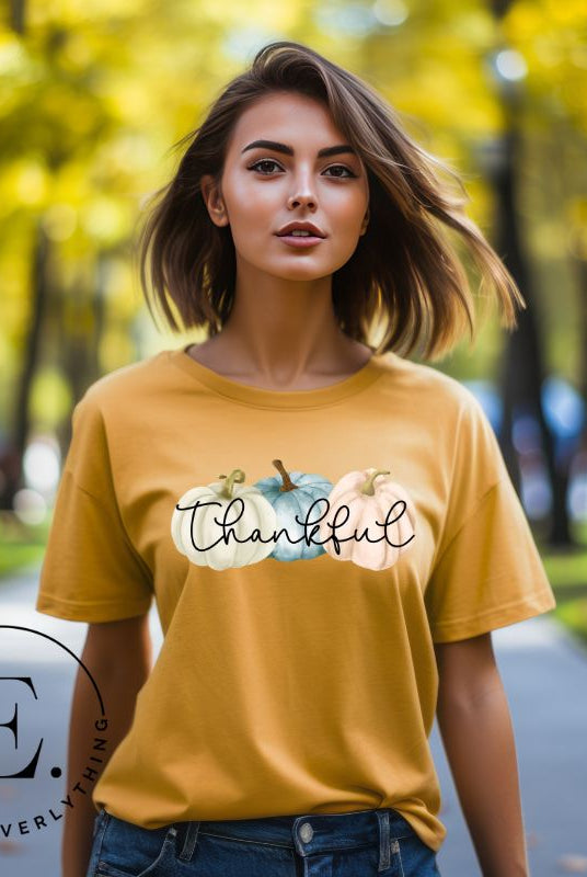 Express gratitude in style with our charming t-shirt. This design radiates autumn appreciation, featuring three pastel pumpkins and the word 'thankful' gracefully woven through the middle on a yellow shirt. 