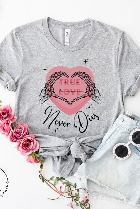 Embrace the unconventional with our Valentine's Day shirt featuring the bold statement "True Love, Never Dies" adorned with a heart and skeleton hands forming a heart shape on grey shirt. 