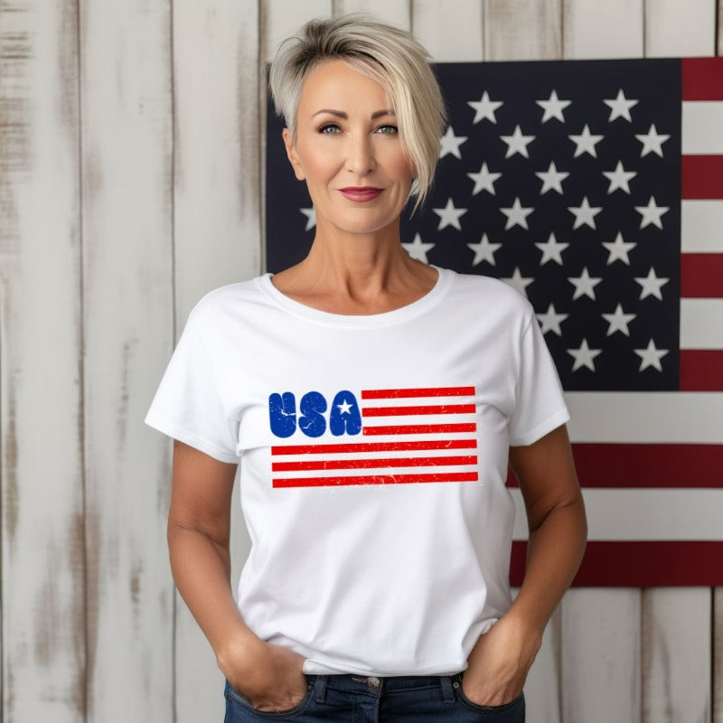 A stylish graphic tee for the USA July 4th celebration featuring a creatively designed American flag. The tee showcases the flag's stripes morphing into the text "USA" while the stars on the flag are creatively incorporated into the design, creating a unique and patriotic look on a white graphic tee.