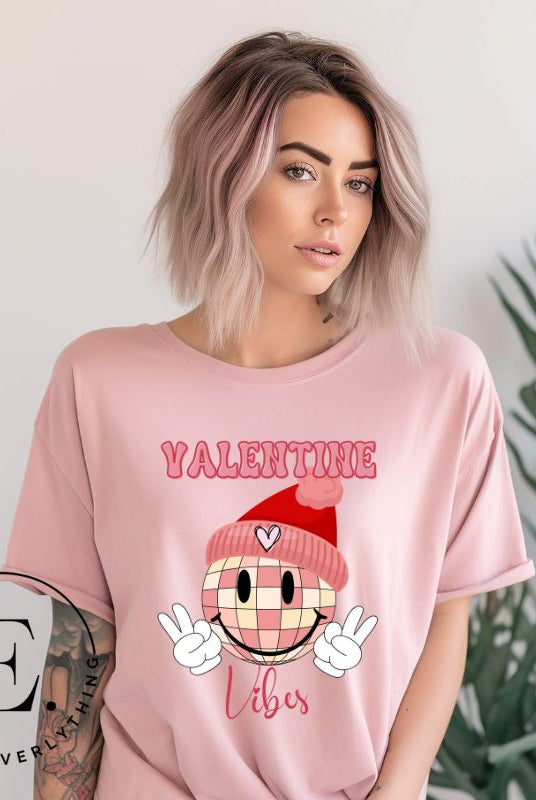 Get into the Valentine's Day spirit with our fun and funky shirt donning the words "Valentine Vibes" alongside a disco ball smiley face flashing peace fingers on a pink shirt. 