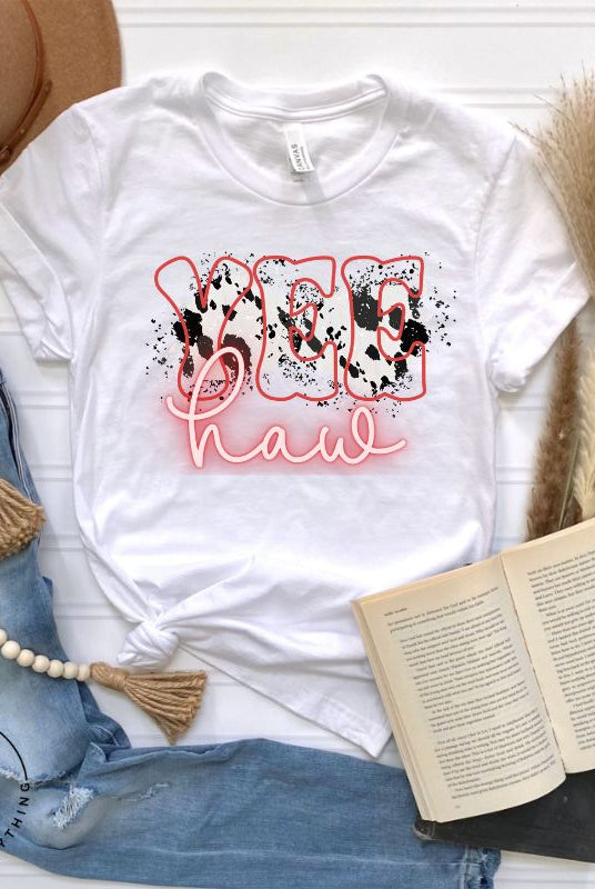 Saddle up in style with our country western shirt featuring the spirited exclamation "Yeehaw" set against a sleek cowhide print background, accented with neon pink lettering on a white shirt. 