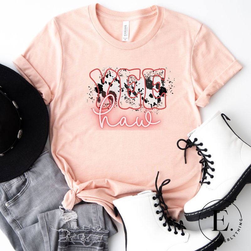 Saddle up in style with our country western shirt featuring the spirited exclamation "Yeehaw" set against a sleek cowhide print background, accented with neon pink lettering on a peach shirt.