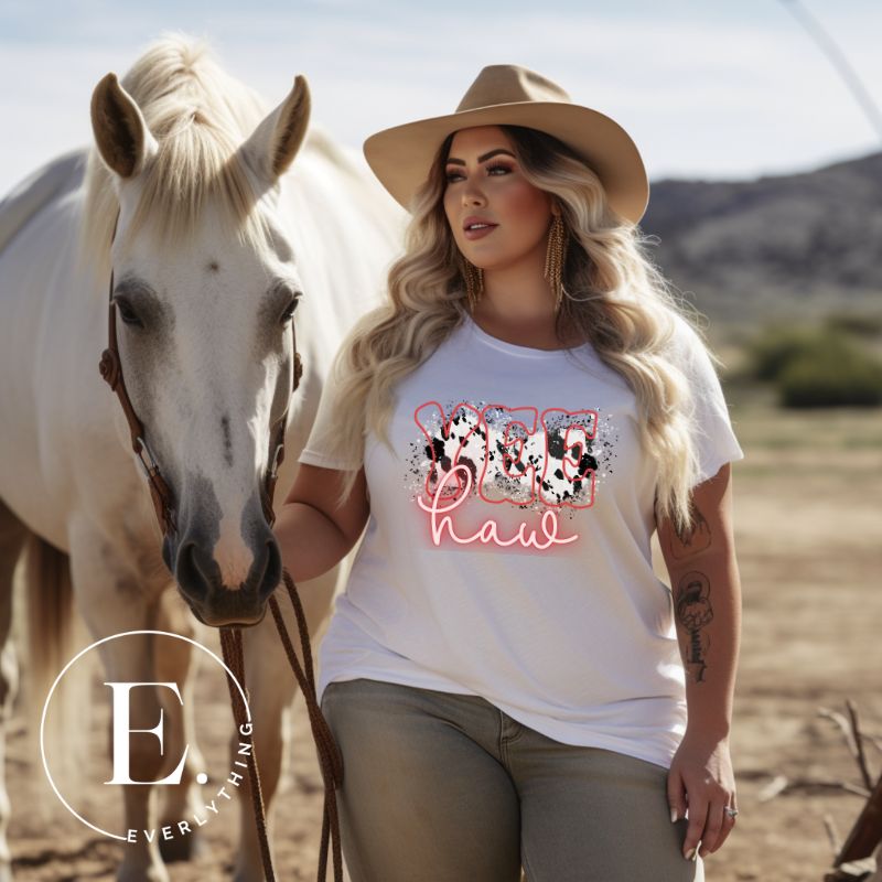 Saddle up in style with our country western shirt featuring the spirited exclamation "Yeehaw" set against a sleek cowhide print background, accented with neon pink lettering on a white shirt. 