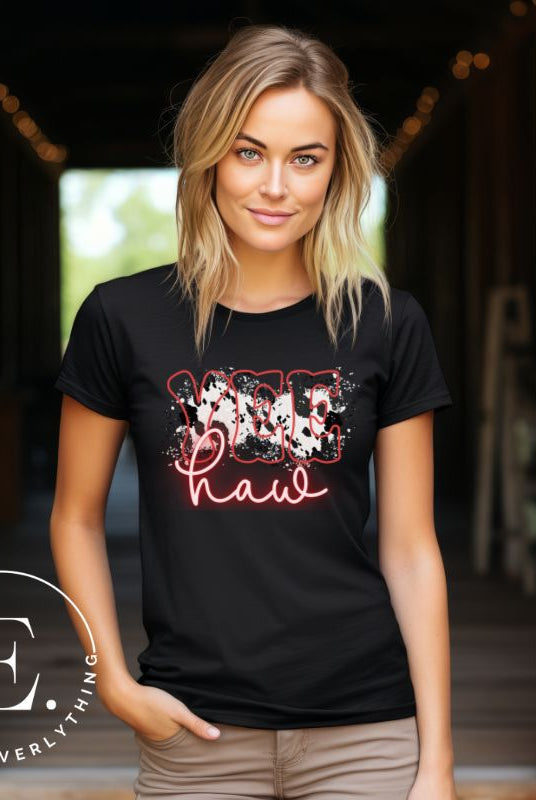 Saddle up in style with our country western shirt featuring the spirited exclamation "Yeehaw" set against a sleek cowhide print background, accented with neon pink lettering on a black shirt. 