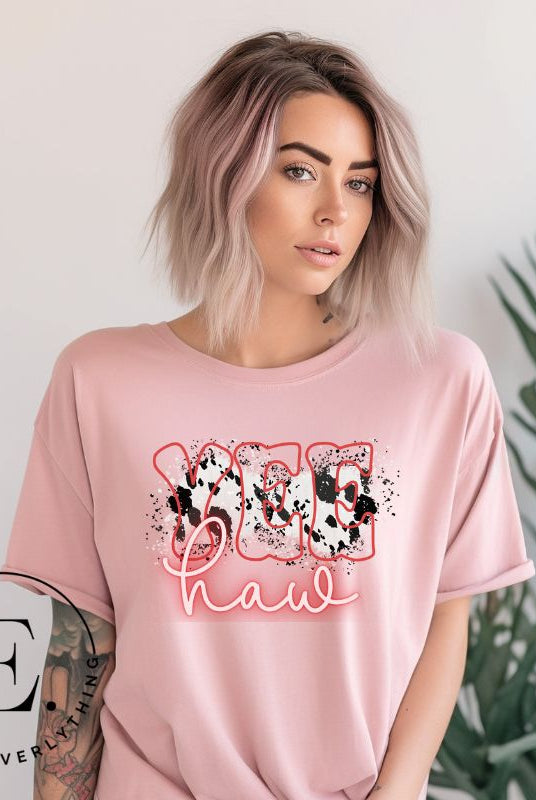 Saddle up in style with our country western shirt featuring the spirited exclamation "Yeehaw" set against a sleek cowhide print background, accented with neon pink lettering on a pink shirt. 