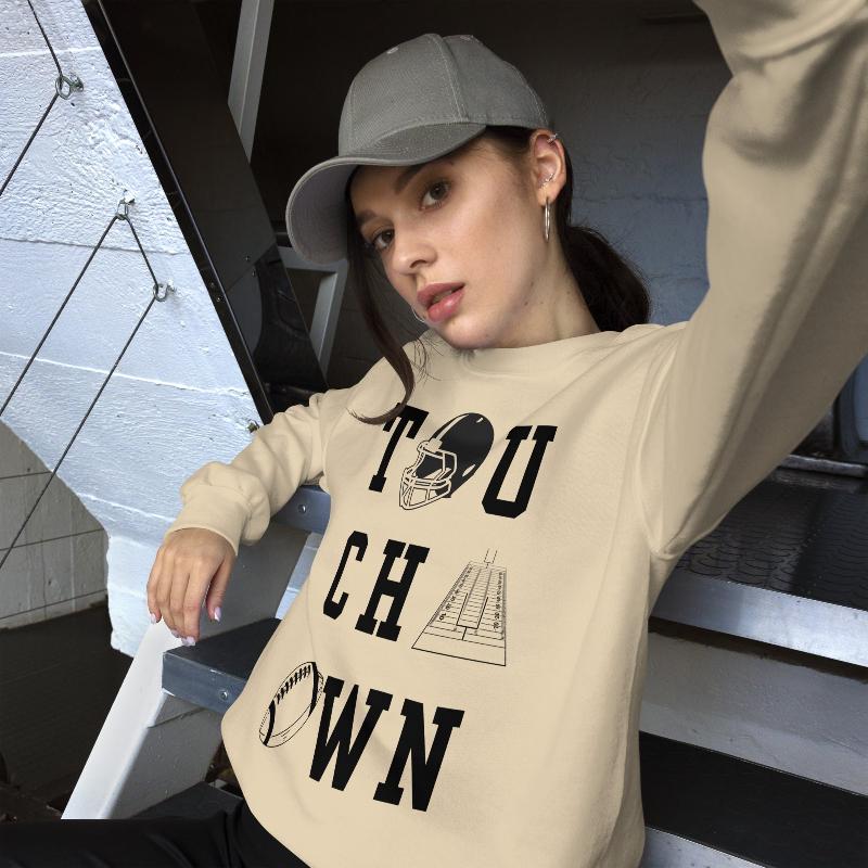 "TOUCHDOWN" letters, featuring a football helmet, field, and football graphics on a beige sweatshirt. 