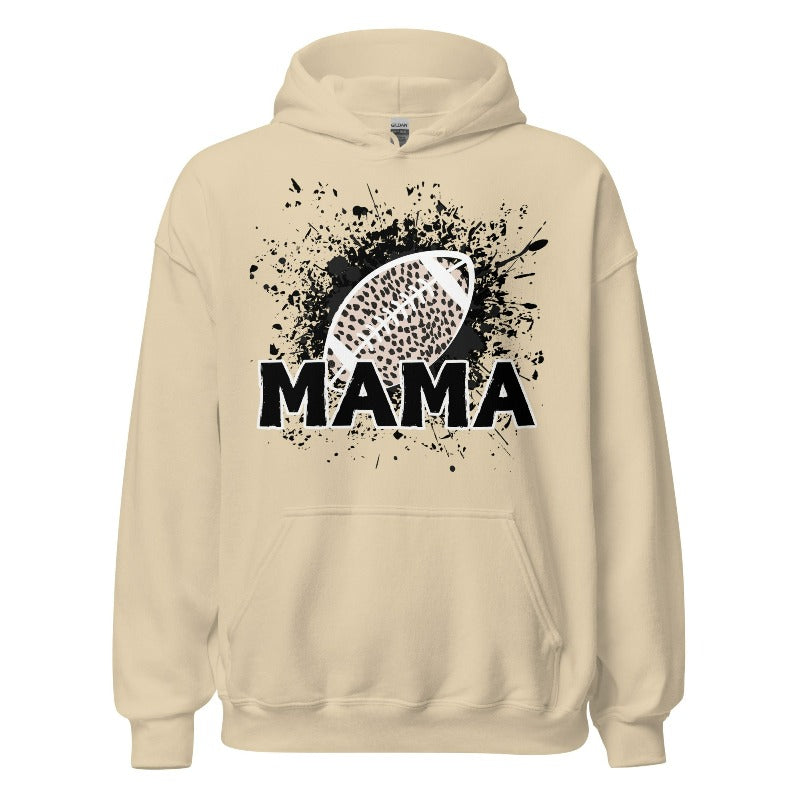 Gildan Hoodie Sweatshirt featuring a cheetah print football graphic with the word "MAMA" in bold black letters underneath, set against a dynamic black splatter background. The hoodie has a front pouch pocket, double-lined hood, and rib-knit cuffs and waistband. This design is on a sand hoodie