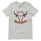 Unleash your cowboy spirit with our country western t-shirt boasting the statement "Not my First Rodeo" alongside bold bull horns and a lasso design on an athletic heather grey shirt. 