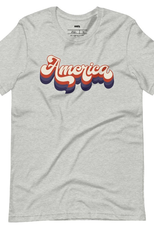 Close-up image of a USA July 4th graphic tee with the word 'America' spelled out in funky retro lettering on the front. This vintage-inspired tee is perfect for adding a fun and nostalgic touch to your Independence Day celebrations on an athletic heather grey graphic tee. 