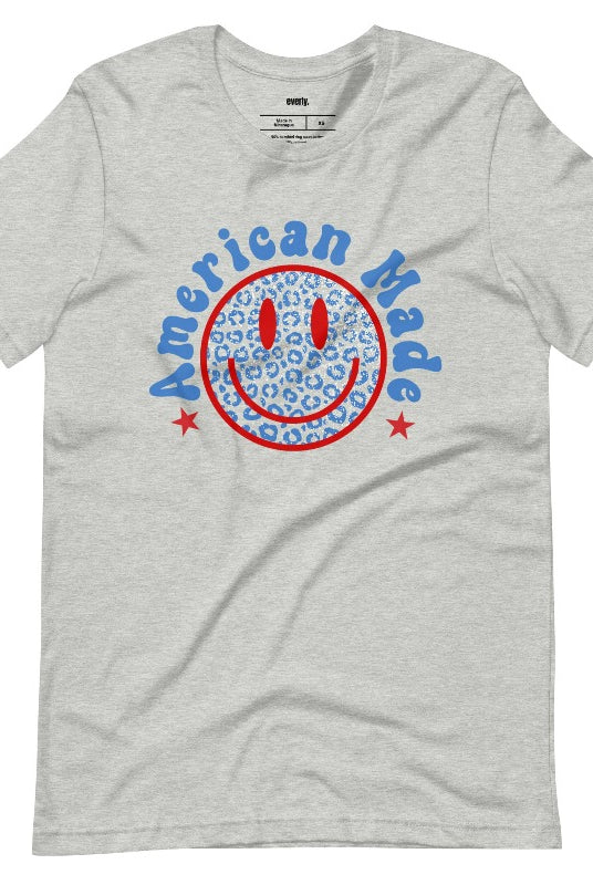 Close-up image of a USA July 4th graphic tee featuring the words 'American Made' surrounded by retro lettering around a bold blue cheetah print retro smiley face on the front. A playful and unique design perfect for celebrating July 4th in style on an athletic heather grey tee.