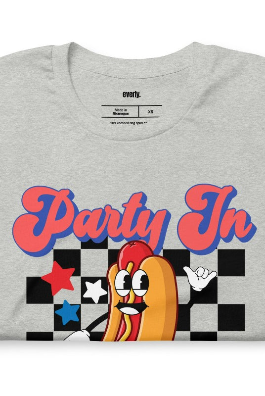 Graphic of a retro-style hotdog with a checkered background, with the text 'Party in the USA' on the front of an athletic heather grey graphic tee.