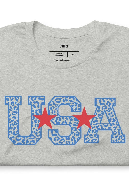 Stylish and bold USA July 4th graphic tee with blue cheetah print 'USA' on the front, adding a trendy and fierce touch to your patriotic wardrobe on a grey graphic tee.
