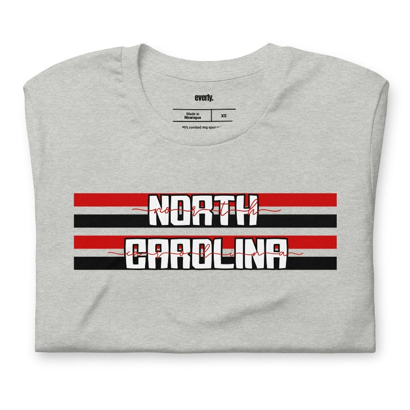 "North Carolina" in bold red and white text on a black and red striped background across the chest on a grey shirt.