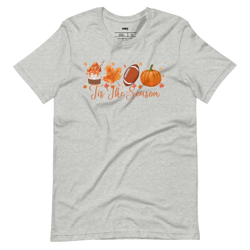  'Tis The Season' design with fall-themed graphics including a cupcake, maple leaf, football, and pumpkin, surrounded by falling leaves on a grey shirt. 