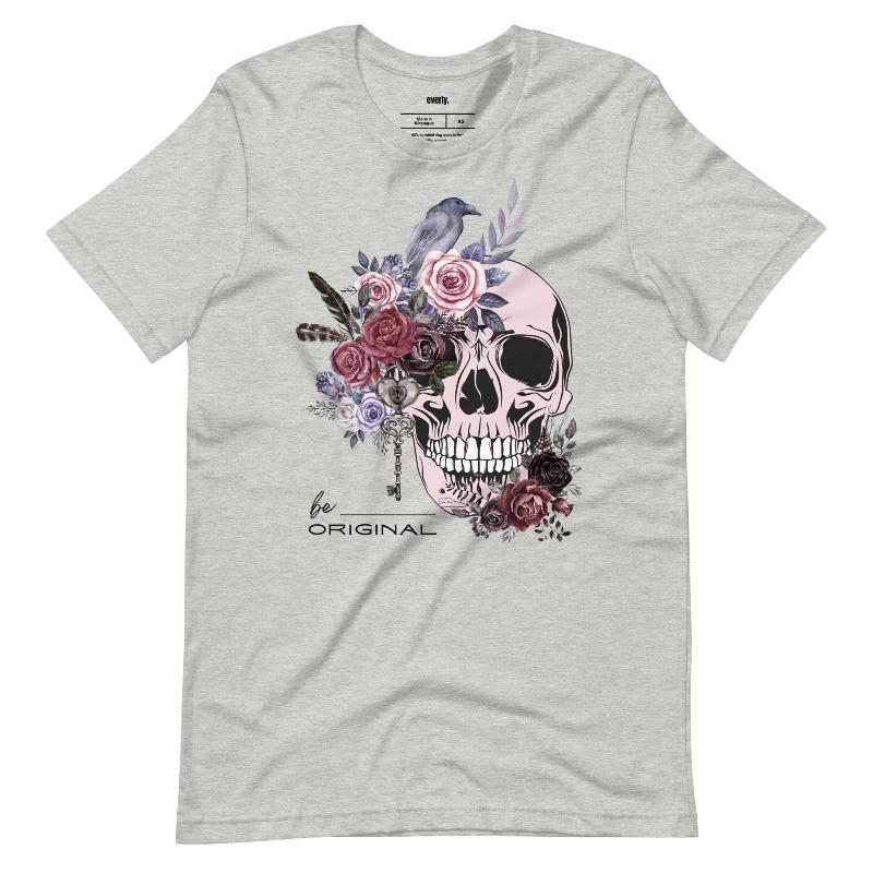 A Halloween-themed design with a skull adorned with flowers and a raven, accompanied by the text "Be Original." The shirt is soft and perfect for celebrating Halloween in style on a grey shirt.