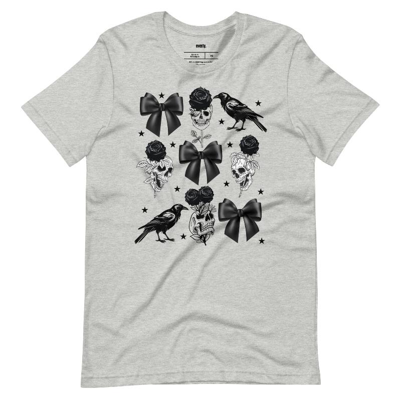 A grey unisex t-shirt featuring a Halloween-themed design with black roses, skulls, ravens, bows, and stars. The design is printed in black and white, giving it a gothic and spooky vibe.