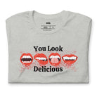 grey t-shirt featuring a graphic of fanged red lips with the playful phrase "You Look Delicious" splattered in red, perfect for Halloween.